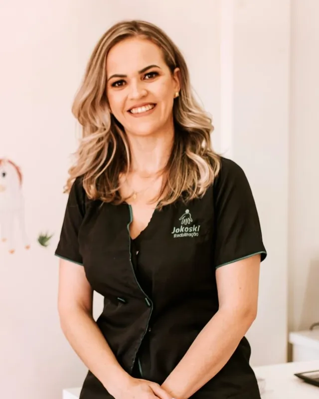 Luciene Jokoski em pé, de braços cruzados à frente, sorrindo, em uma sala clara da clínica